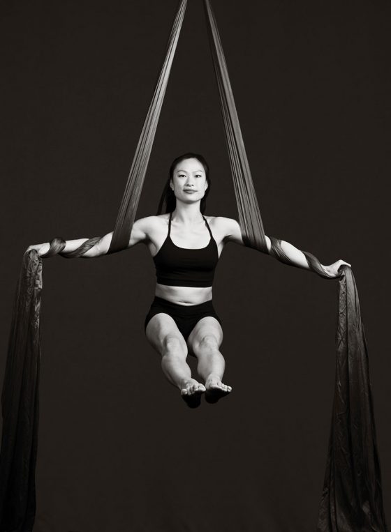 Black and white portrait of Sydney circus aerial silks dancer Katherine Huang, mid air supported by silks.