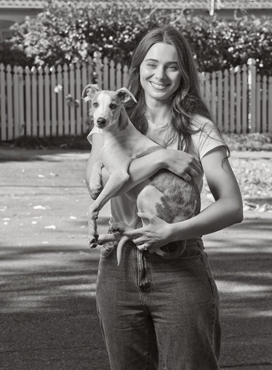 Black and white portrait of Amy holding her dog, while on her driveway in Wahroonga for Fine Photography's COVID vaccination campaign 'Our Call to Arms'.