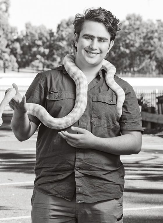 Black and white portrait of Christian, with a snake draped over his neck, taken outside his home in Narwee for Fine Photography's COVID vaccination campaign 'Our Call to Arms'.